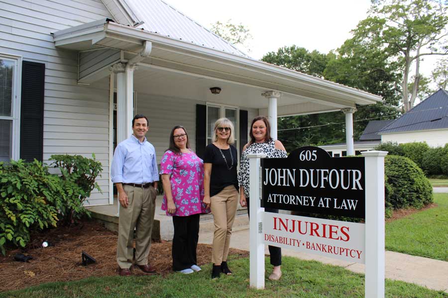 group photo of attorney John Dufour and support staff with law firm sign